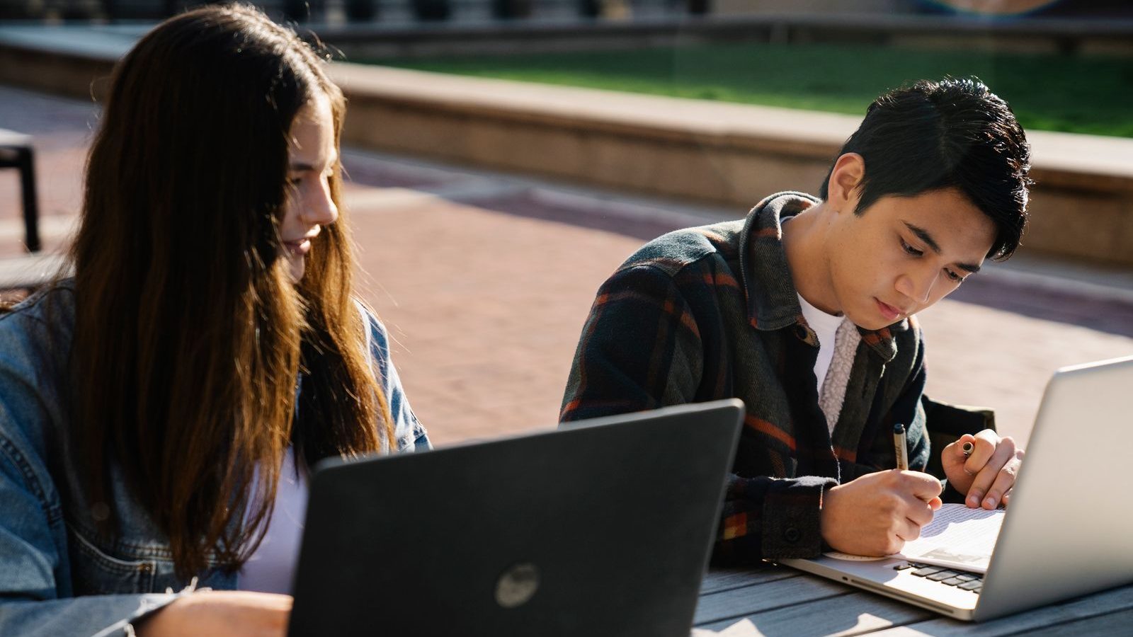 Aspirantes tomando notas y usando laptop en el campus.